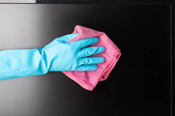 Gloved hand using a microfiber cloth to clean a TV screen.